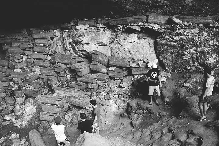 Foto en blanco y negro del interior de la cueva, mostrando ataúdes y una pared hecha de piedras.