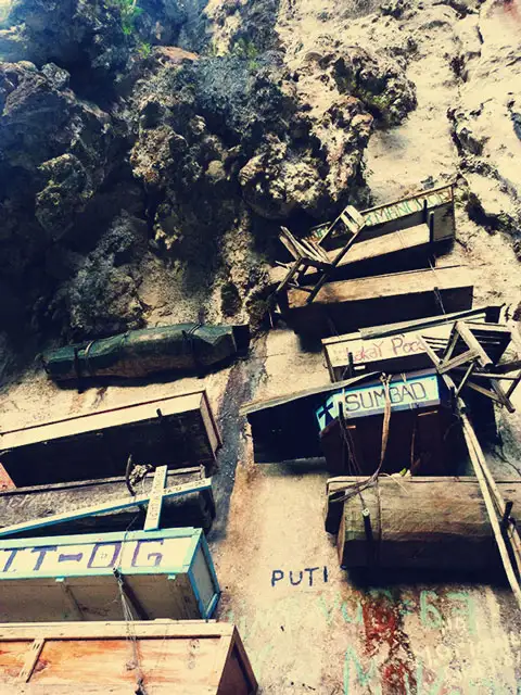 Varias sillas de madera cuelgan junto a sus respectivos ataúdes.