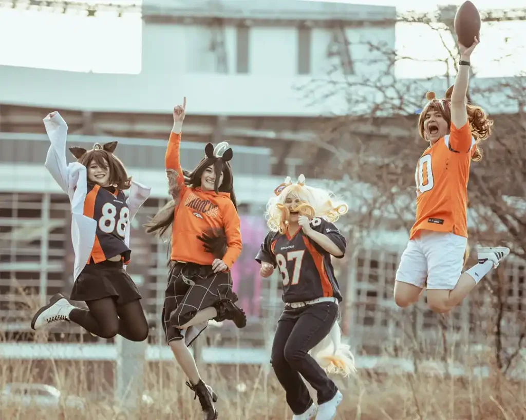 Cuatro cosplayers de Umamusume visten uniformes de los Broncos de Denver mientras saltan para posar en una foto.
