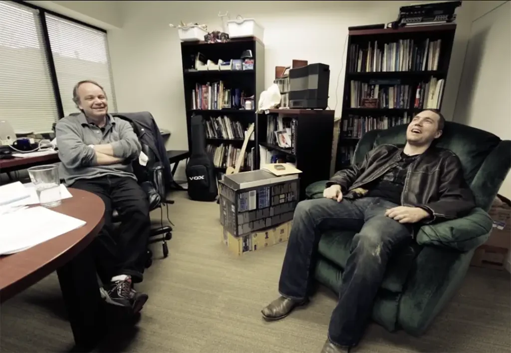 Jake Solomon rie sentado en la silla reclinable verde junto a su mentor Sid Meier.